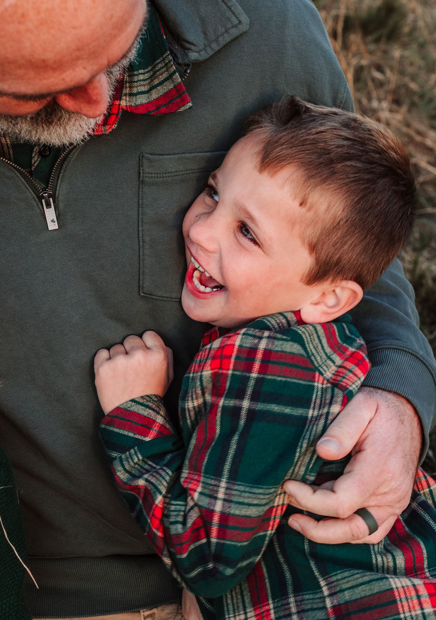 Happy young boy in red plaid shirt laughs while being embraced by a bald man during a family photo session.