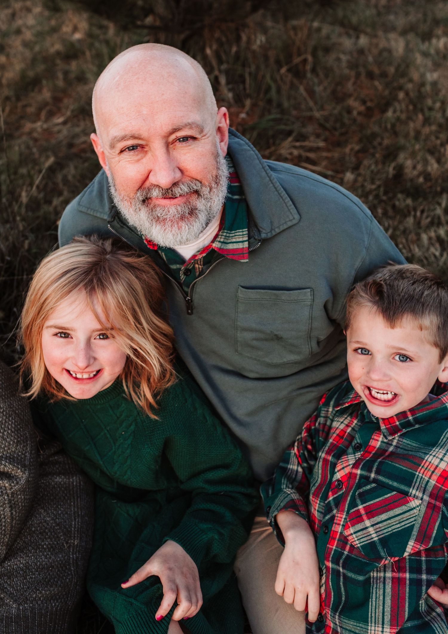 Father smiles with two young children in green and plaid outfits during a holiday photo session.