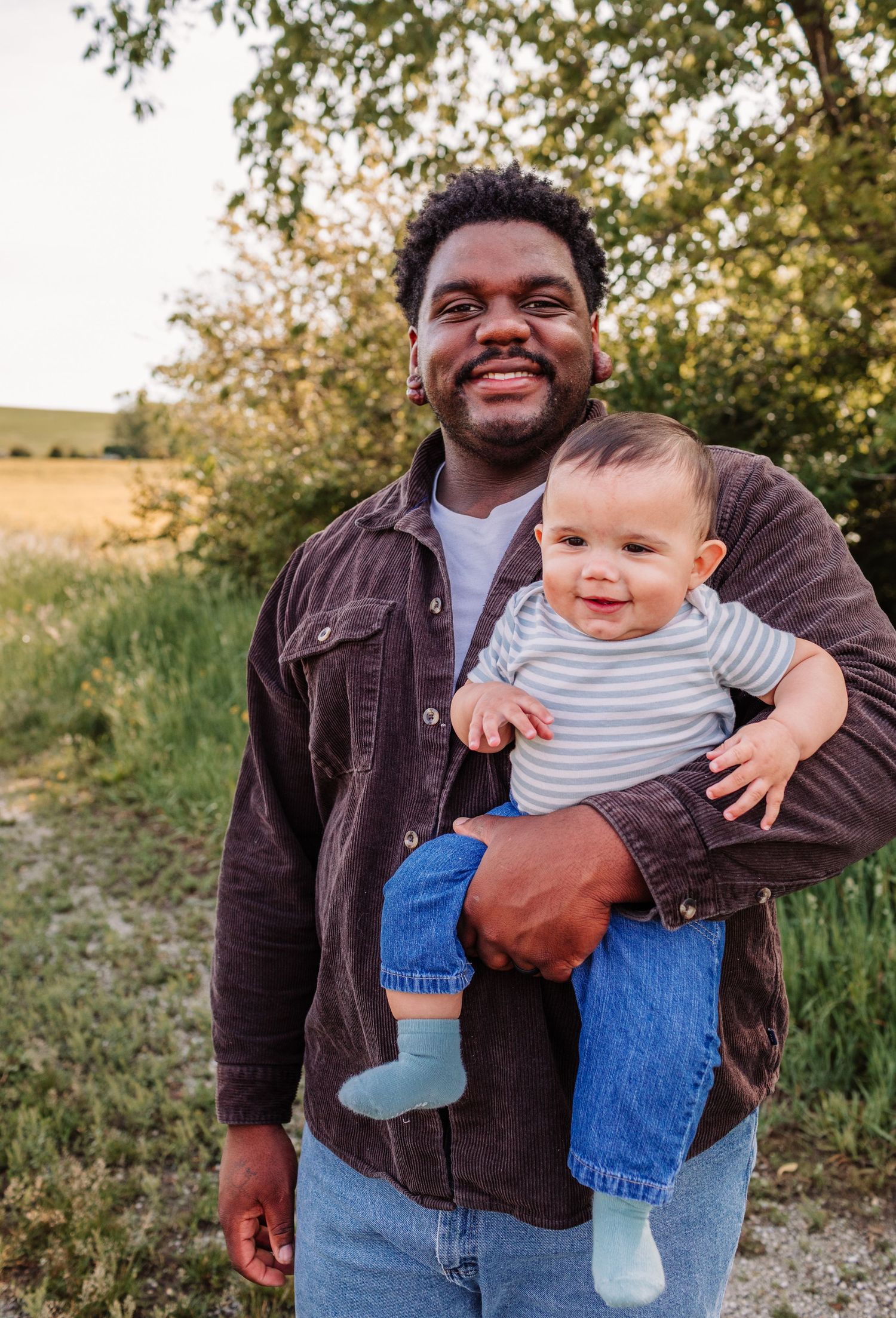 Smiling man holding a happy baby outdoors in a green field during golden hour.