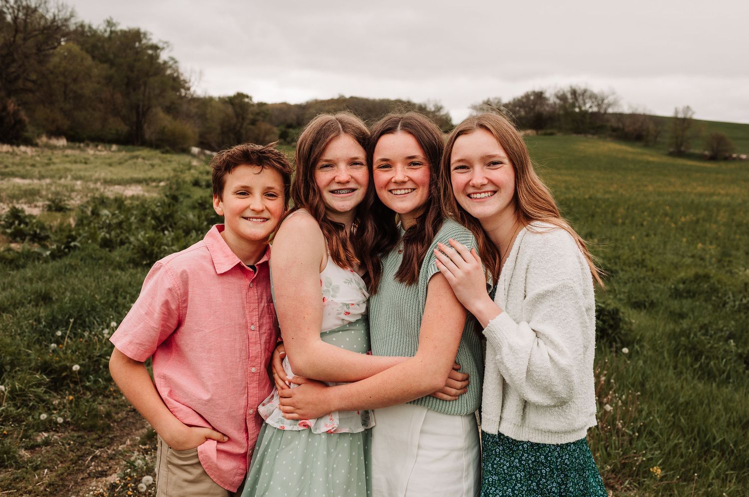 Four siblings hugging and smiling together in a lush green field.