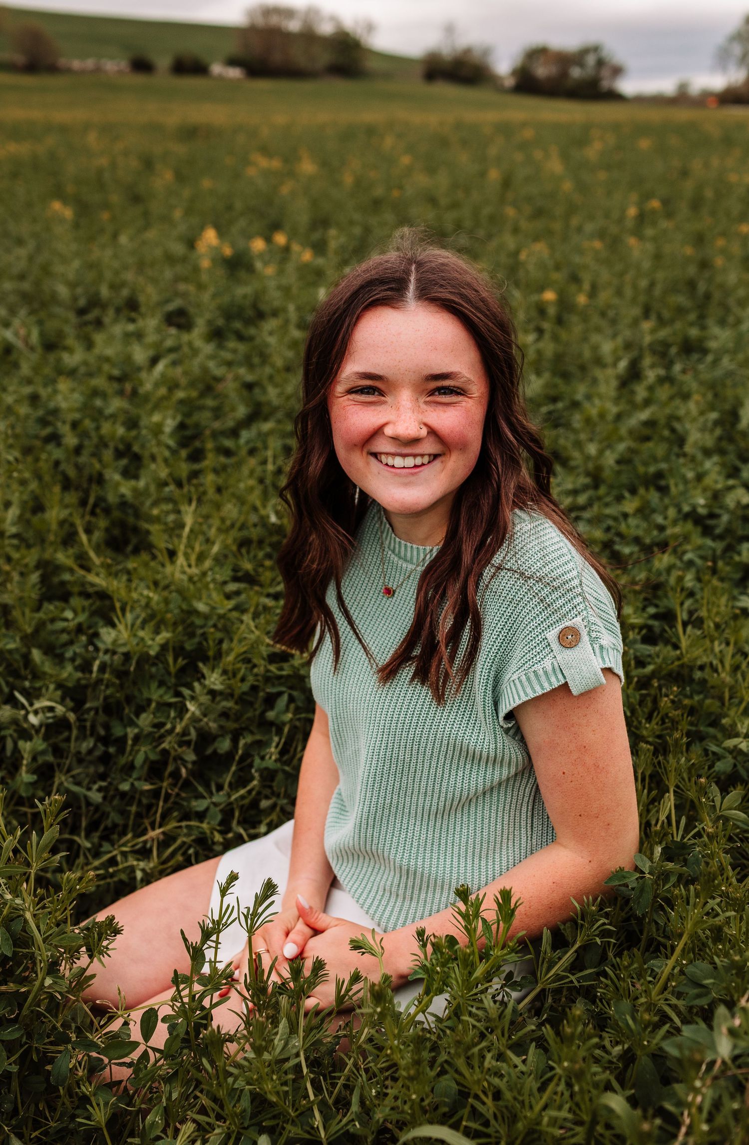 Smiling teenage girl sitting in a green field wearing a mint ribbed top.