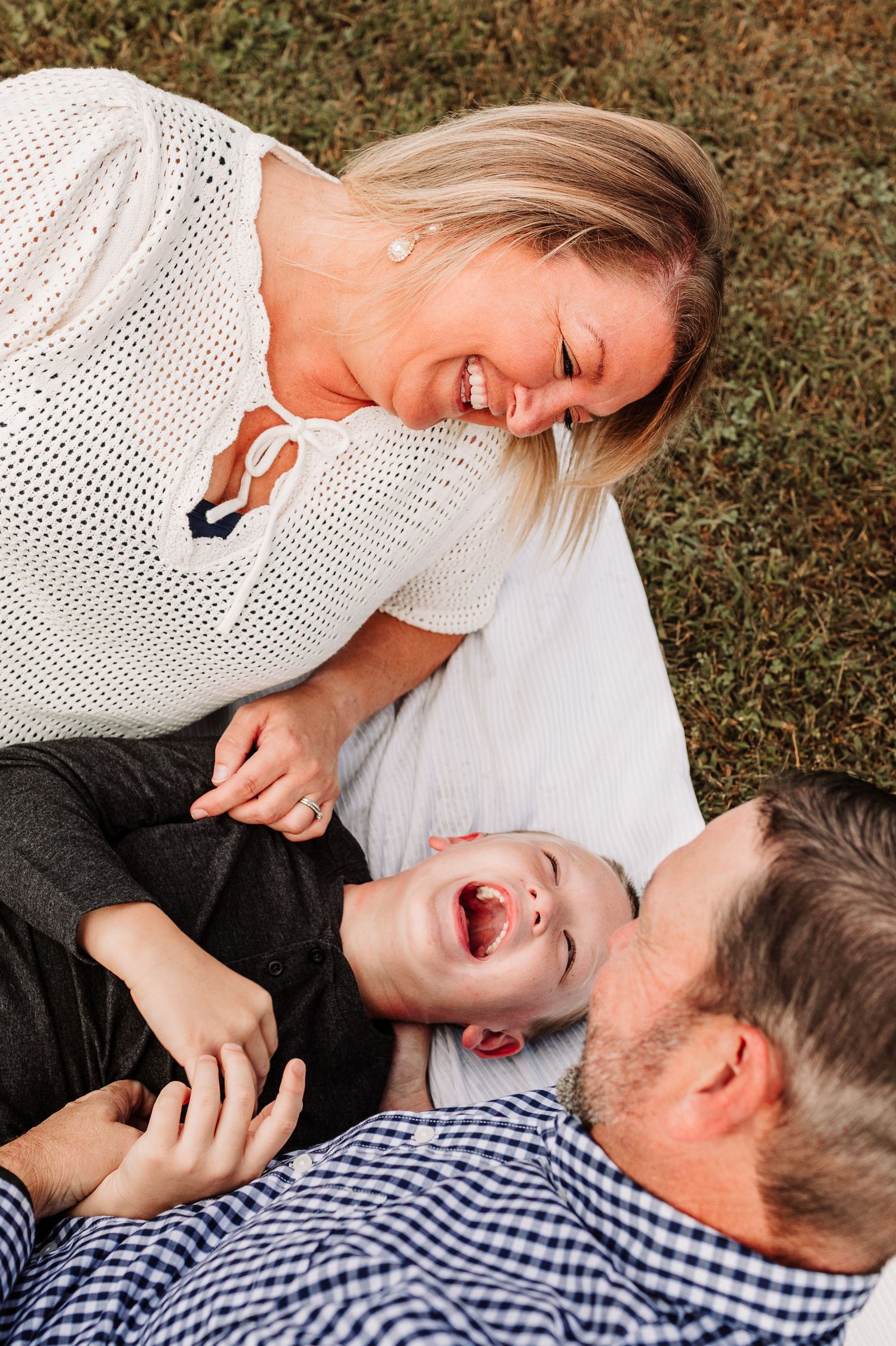 Happy family lying on grass laughing, mother and father playing with young son.