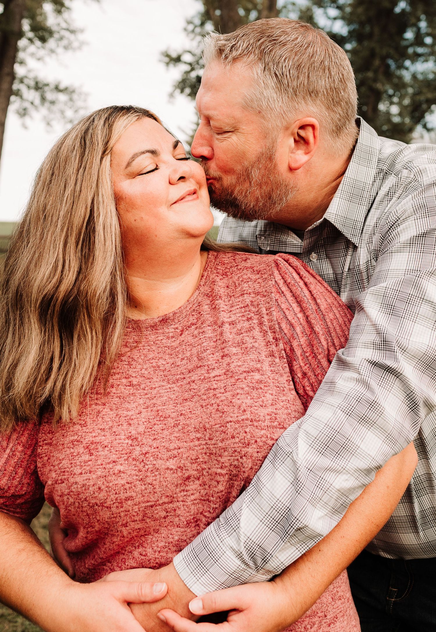 Couple sharing a romantic kiss outdoors among trees.