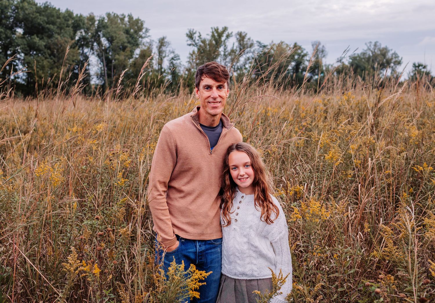 A teenage boy and young girl smiling together in a golden autumn field surrounded by wildflowers.