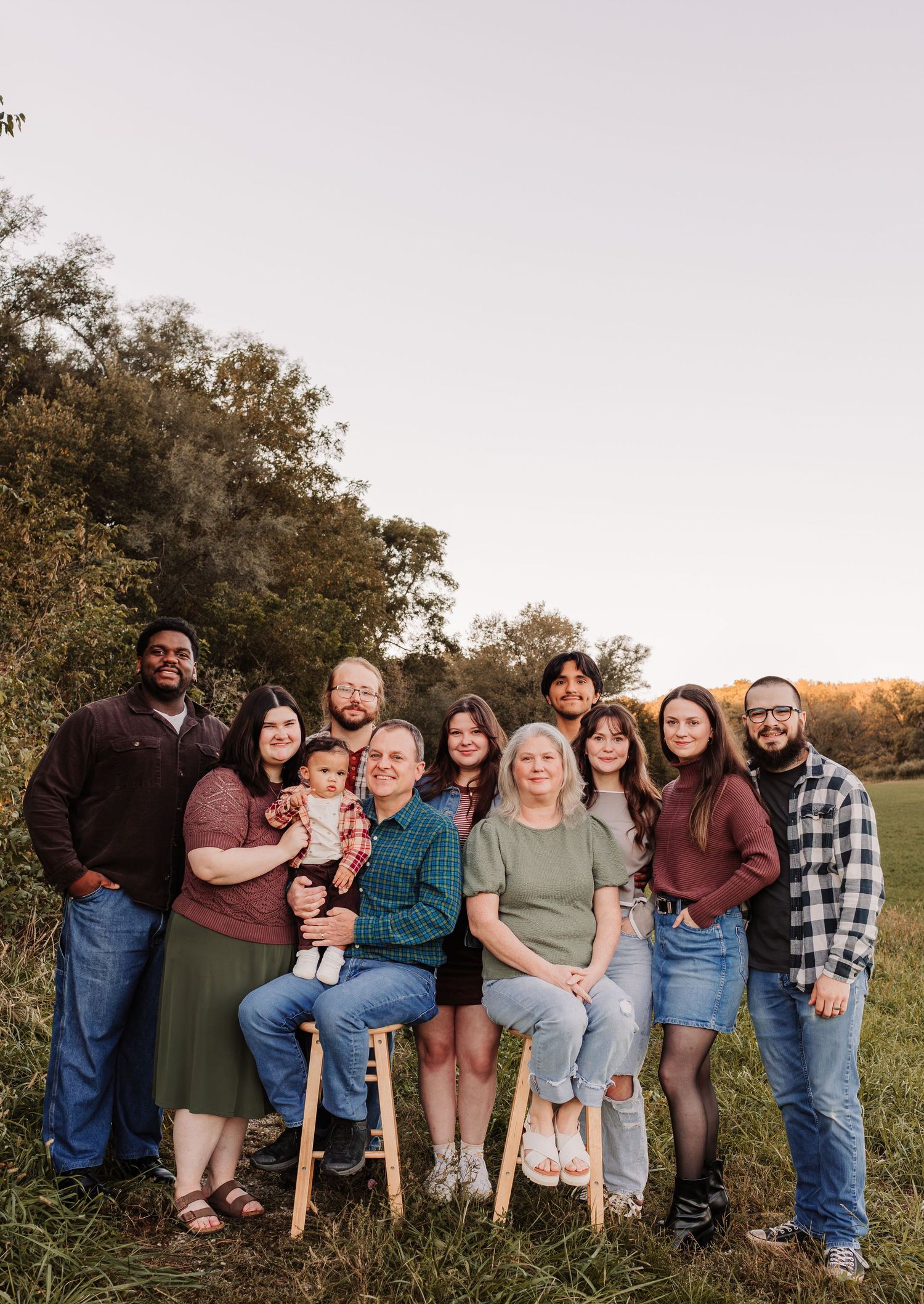Large multigenerational family group portrait outdoors in a green field at golden hour sunset.