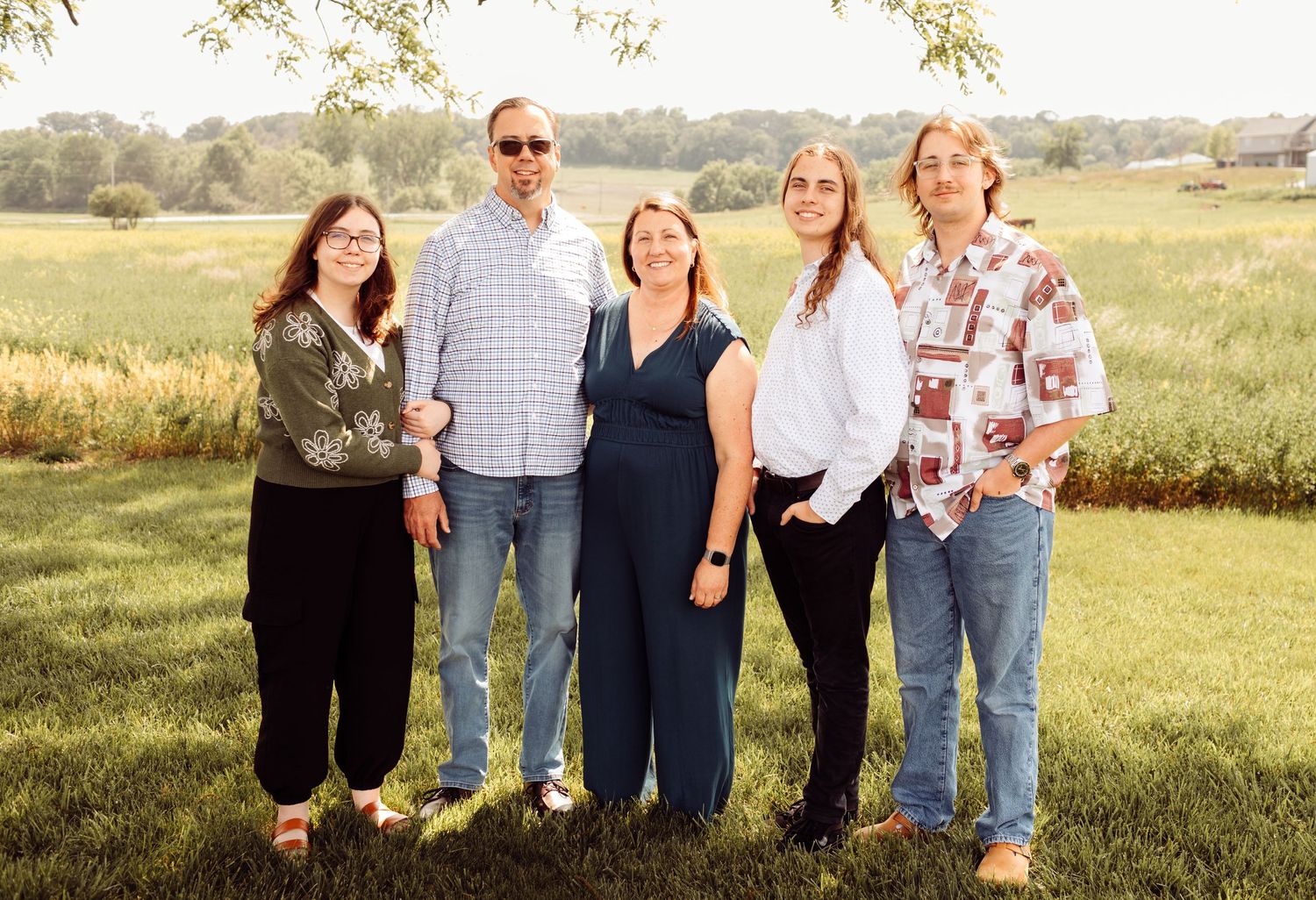 Family of five poses together smiling in a green field during a sunny outdoor photo session.