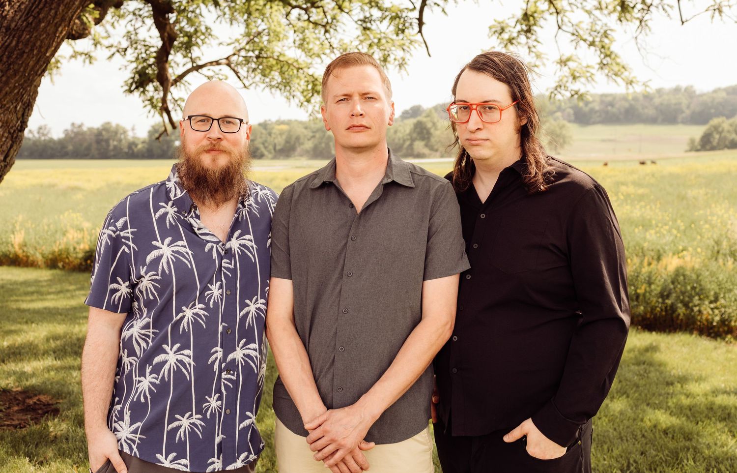Three men posing together outdoors in a green field during golden hour photography session.
