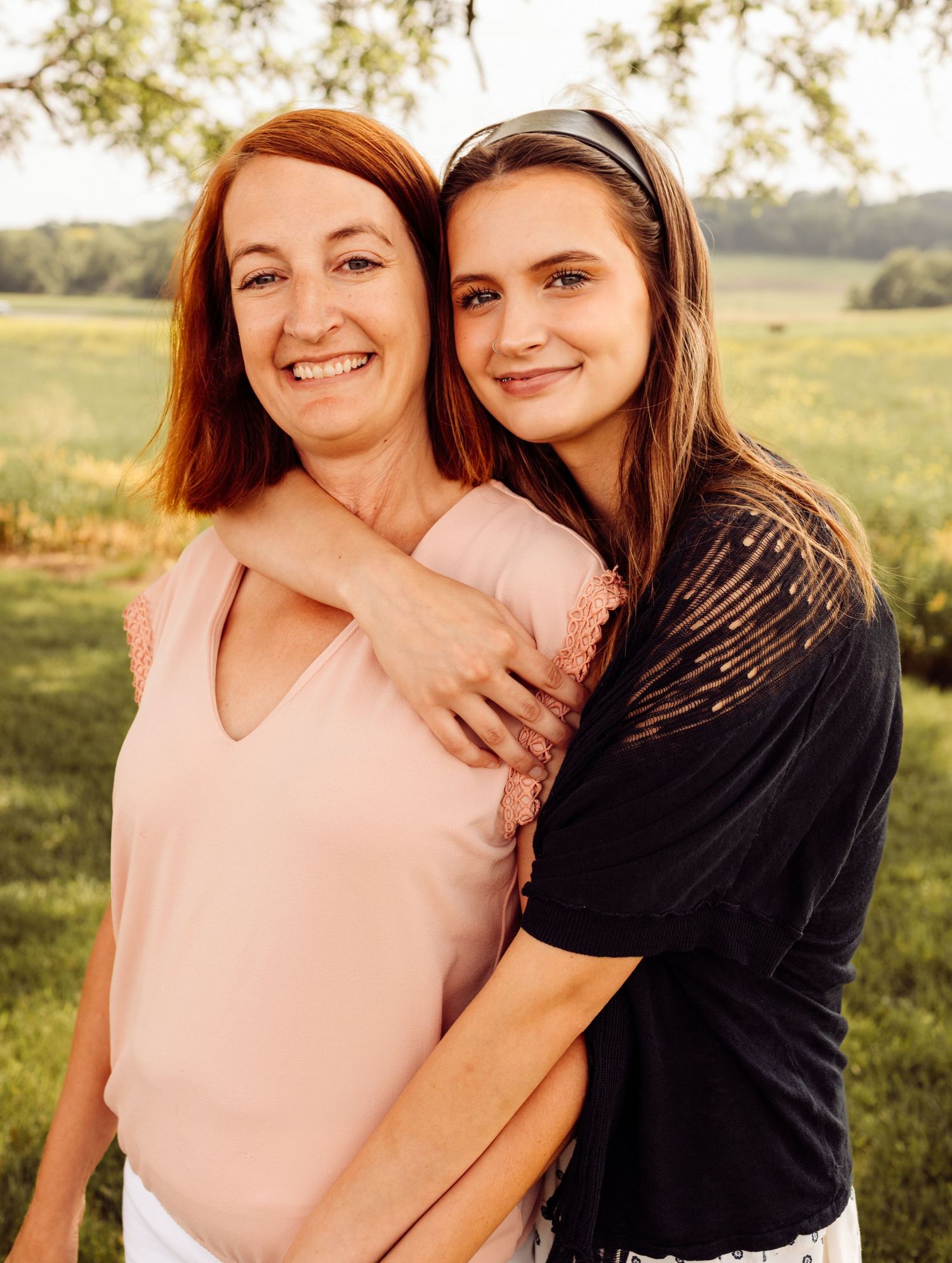 Mother and daughter smiling together outdoors under a tree during a golden hour family portrait.
