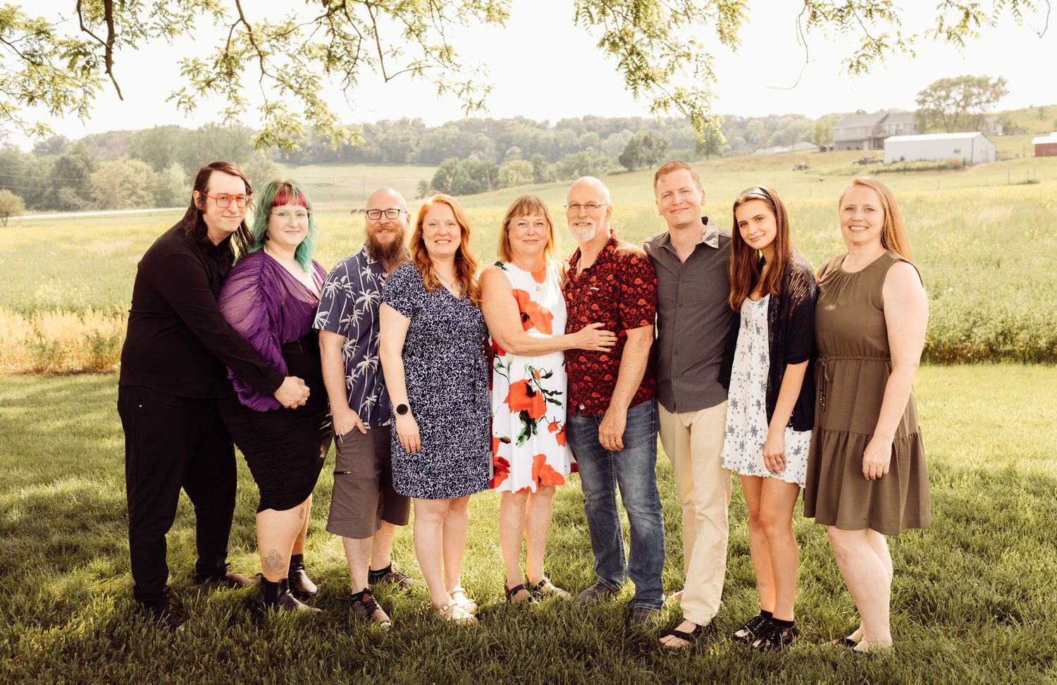Extended family group of eight posing together outdoors in a green field at golden hour.