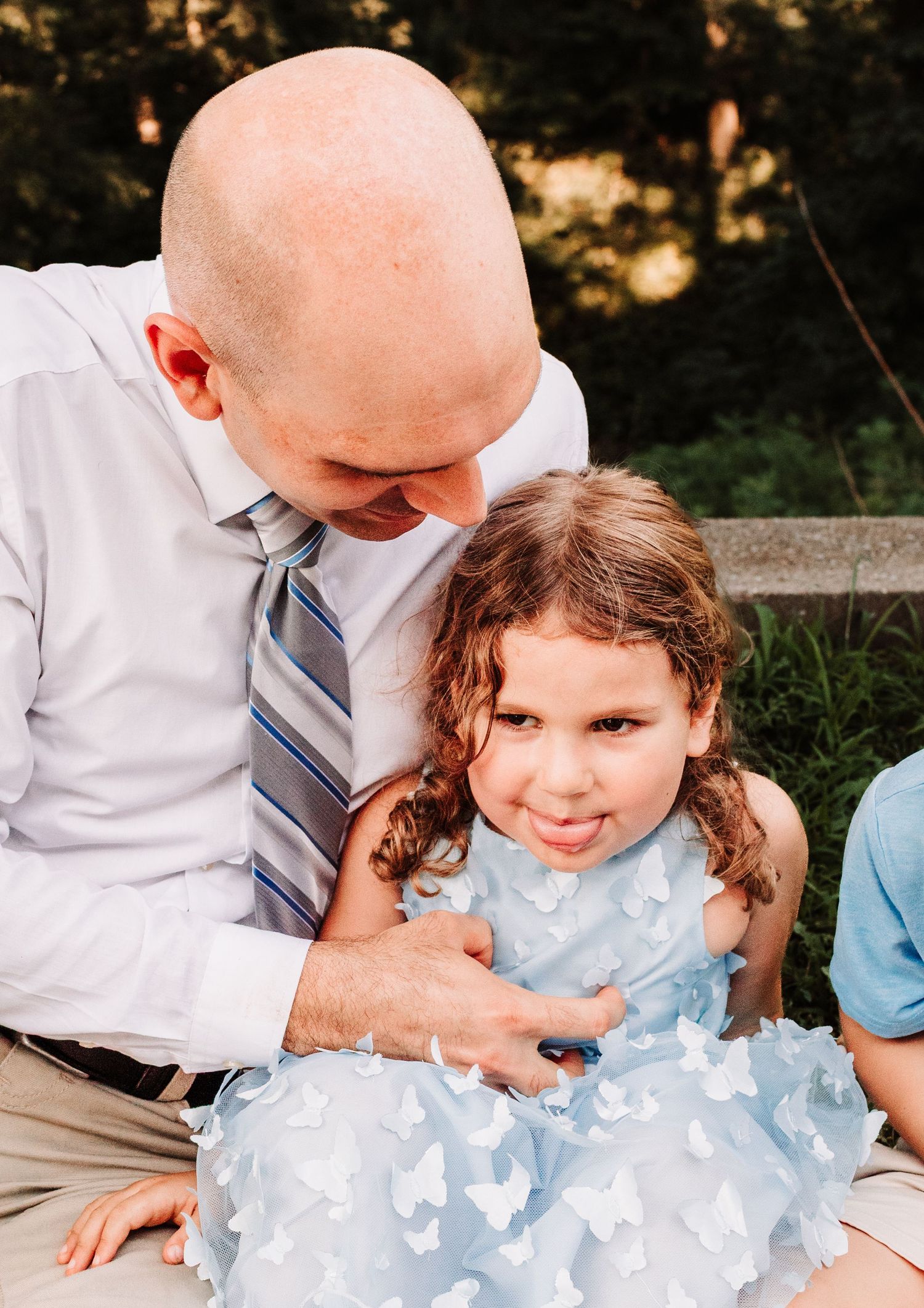 Father in white shirt and tie smiling down at his young daughter in a blue dress.