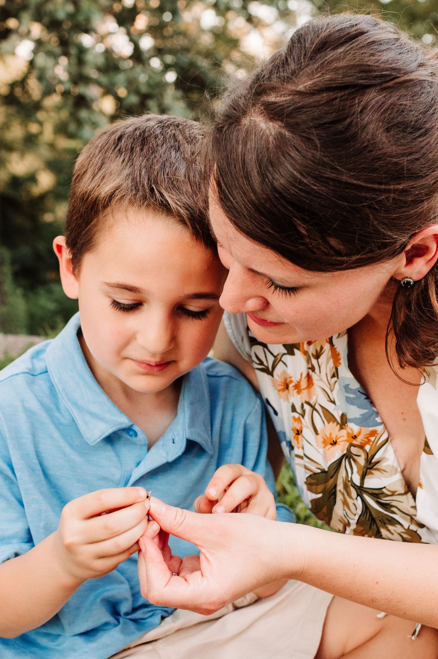 Mother and young boy examining a small object together in a tender outdoor moment.
