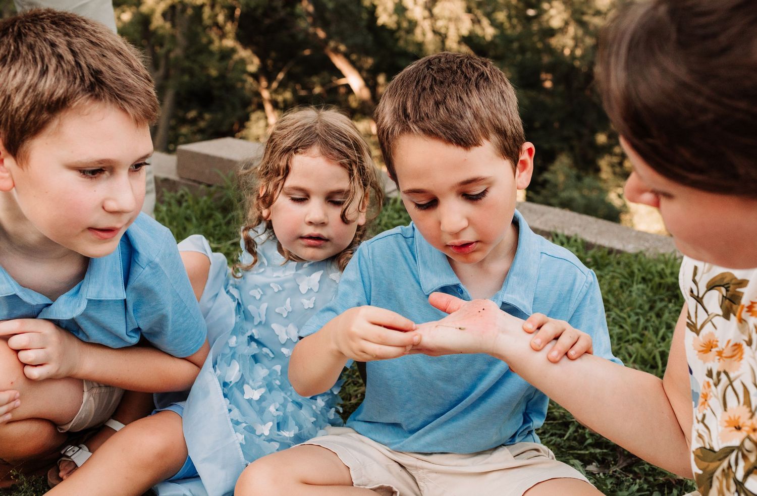 Family group of children and mother examining something small in a childs hand outdoors.