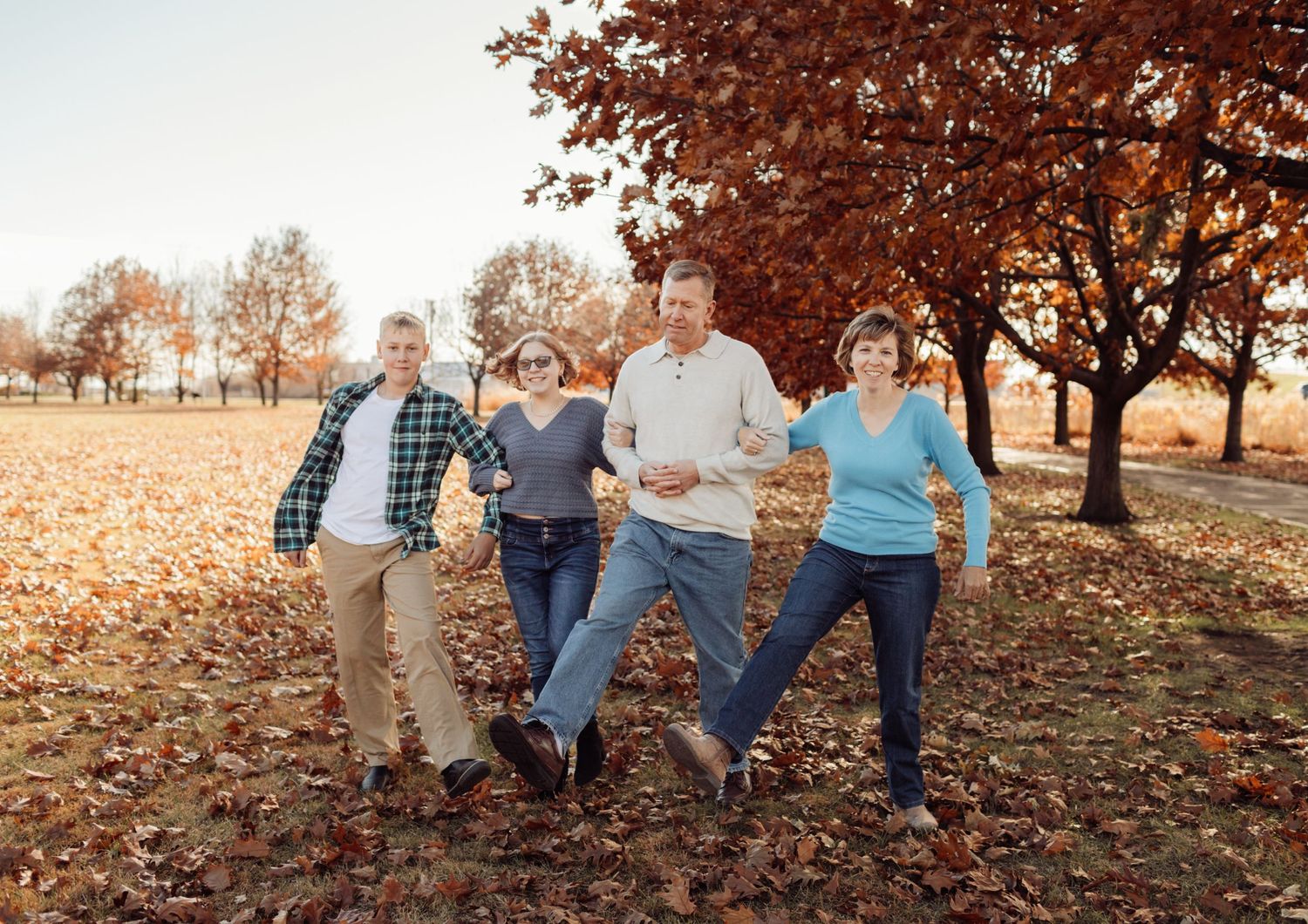 Family of four playfully dancing in an autumn park surrounded by colorful fall foliage.