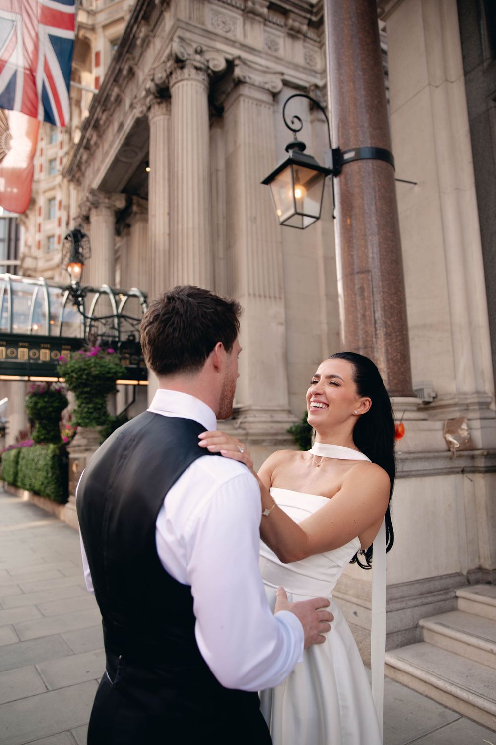 A joyful couple dances and embraces outside a grand building with columns and flags.