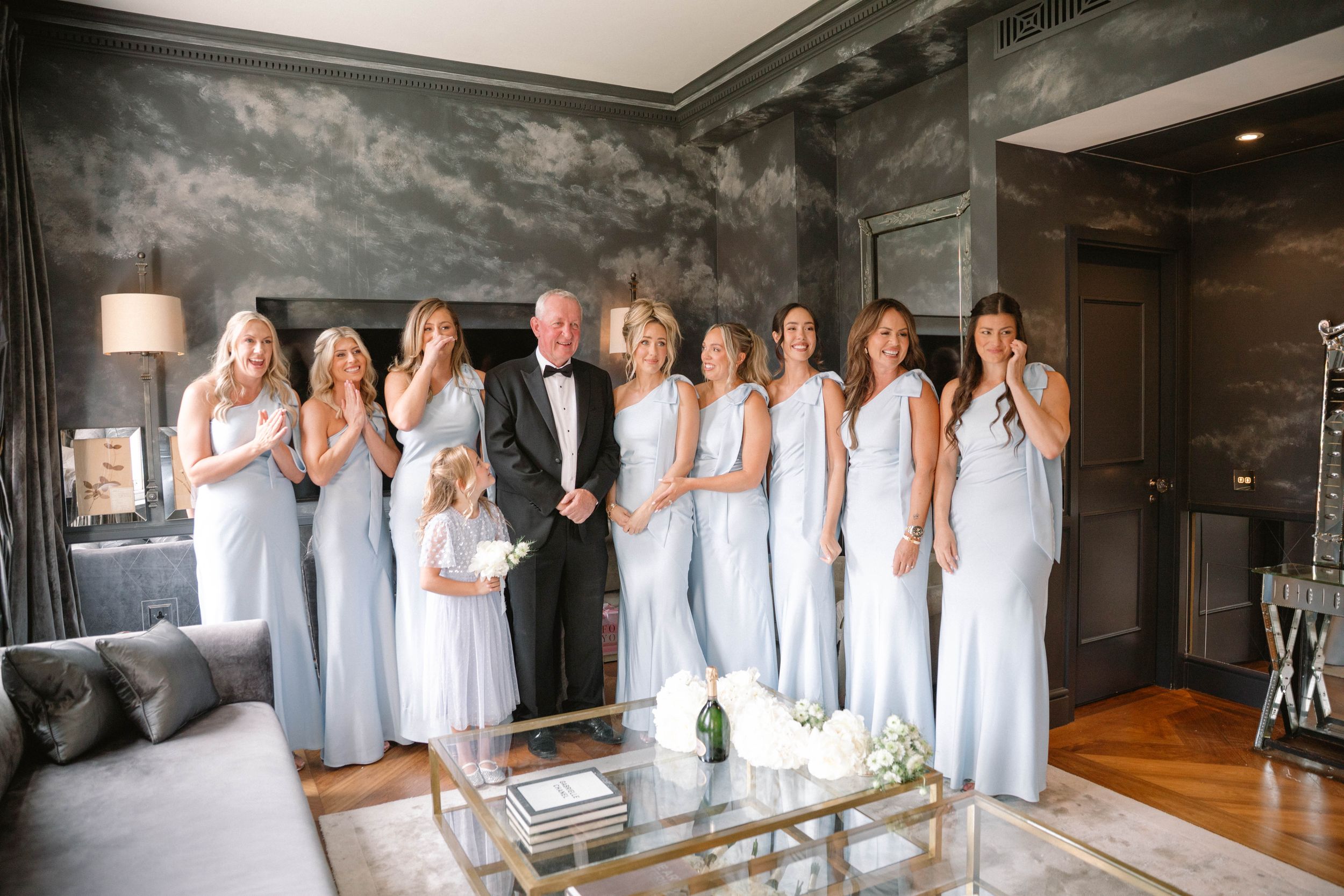 A group in coordinated white outfits gathers in an elegant living room with modern decor and grey walls.