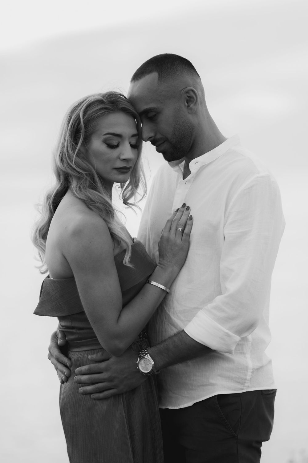 Black and white photo of a romantic couple embracing tenderly, man in white shirt holding woman in strapless dress close.