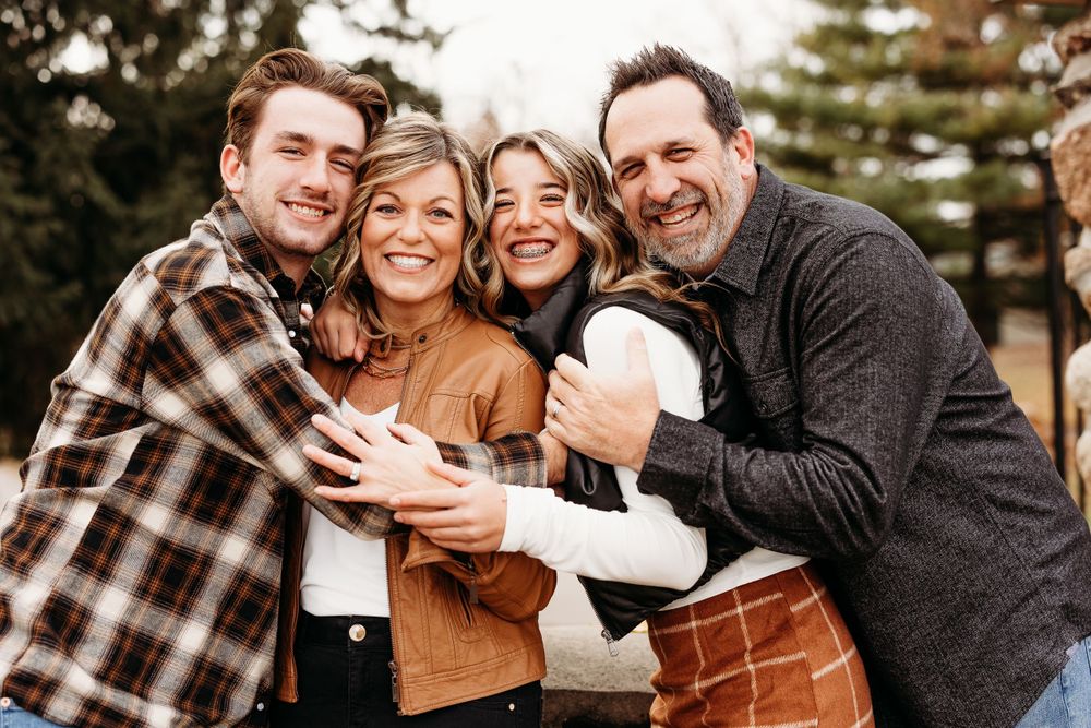 A group photo of four people hugging and laughing together on a wooden bridge.