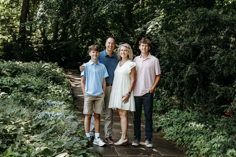 A family of four poses together on a wooded trail surrounded by lush greenery.