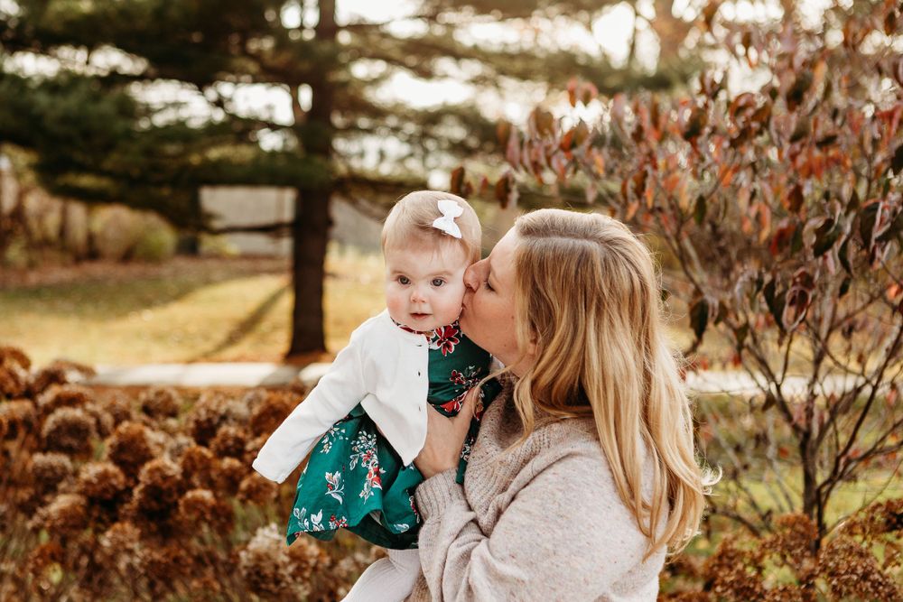 Parent giving a sweet kiss to a baby in a green dress during fall photo session.