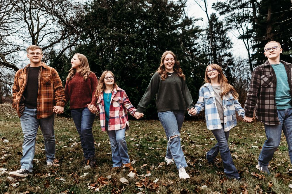 A playful family holding hands together while walking through fallen autumn leaves.