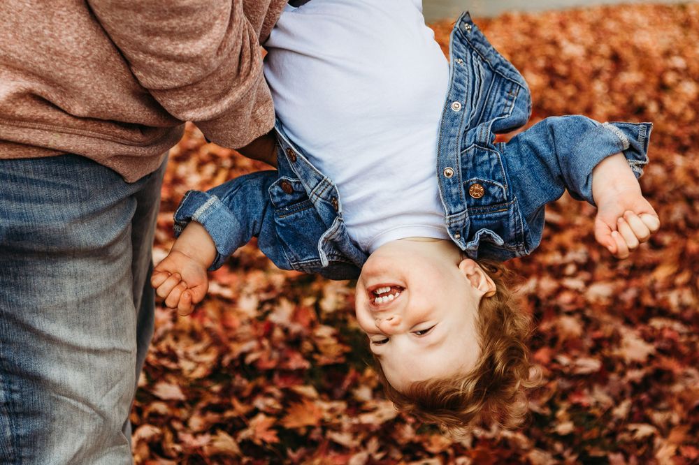 Joyful child being held upside down over fallen autumn leaves.