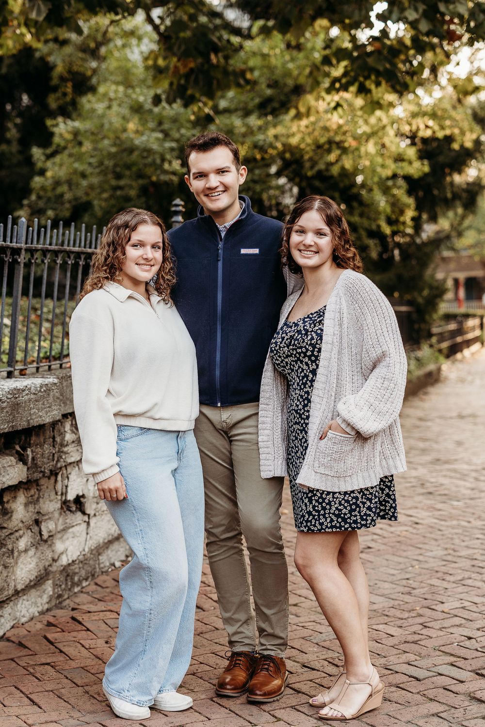 Three people pose together on brick pathway near decorative iron fence.