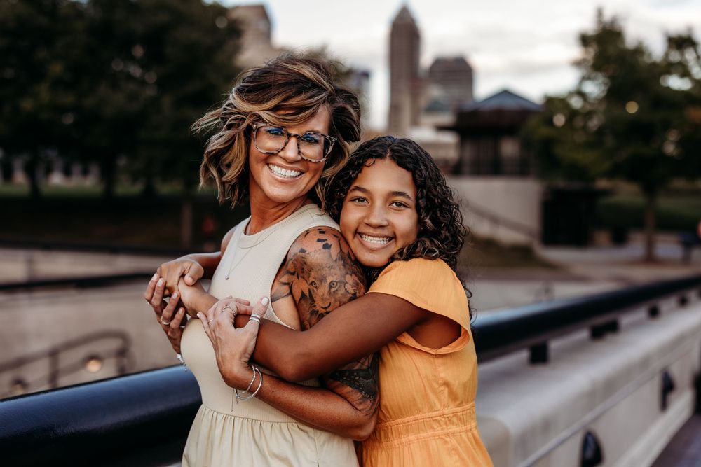 Two friends embrace on city bridge during sunset photoshoot.