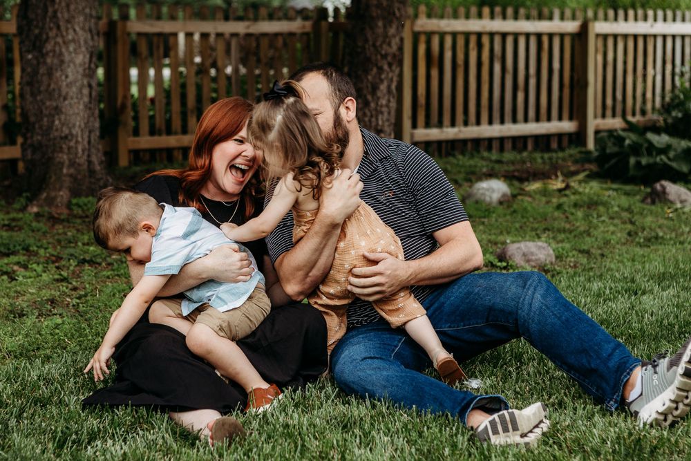 Joyful family sharing laughter while relaxing together on grass in fenced backyard.