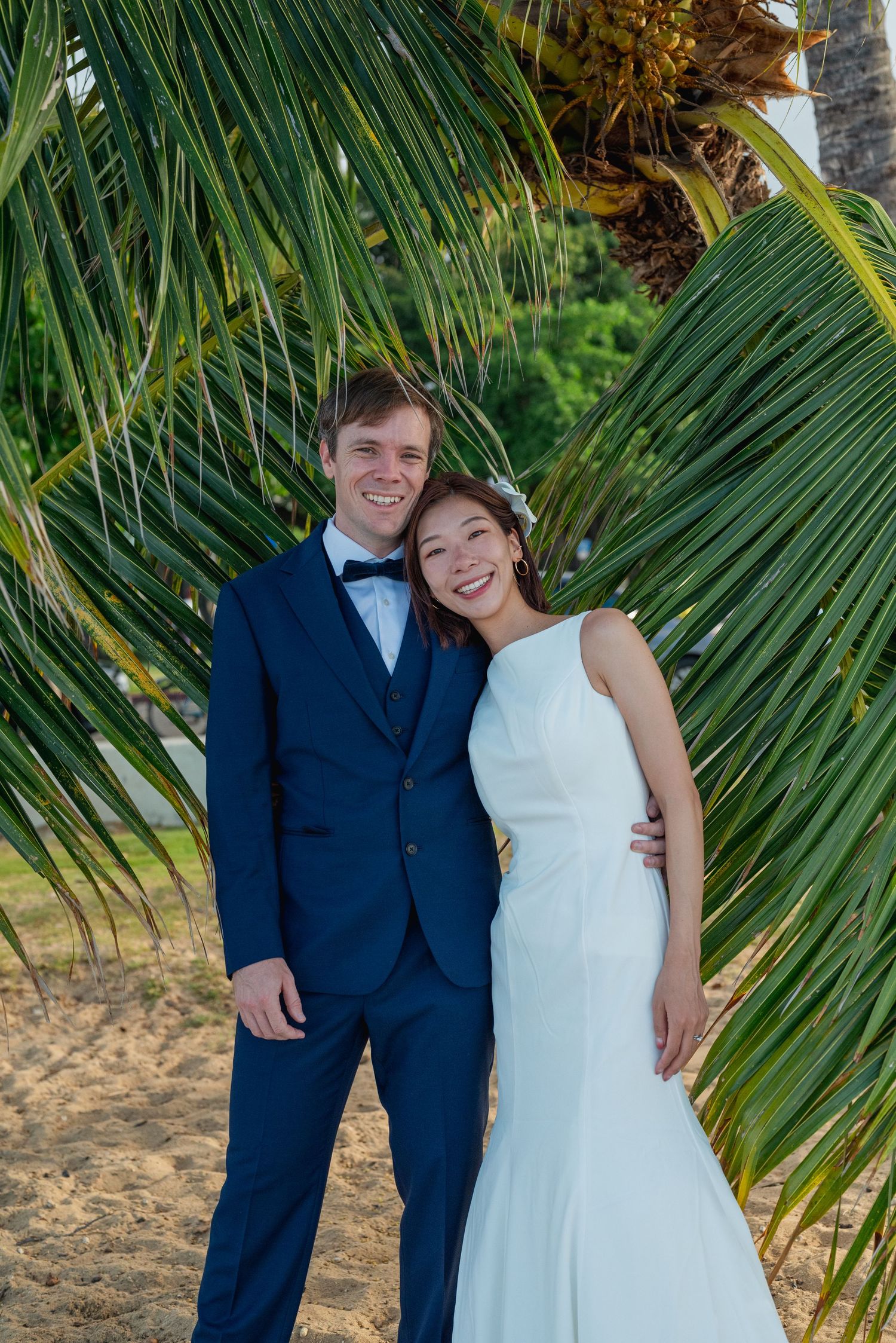 Bride and Groom holding hands under palm tree leaves on a beach