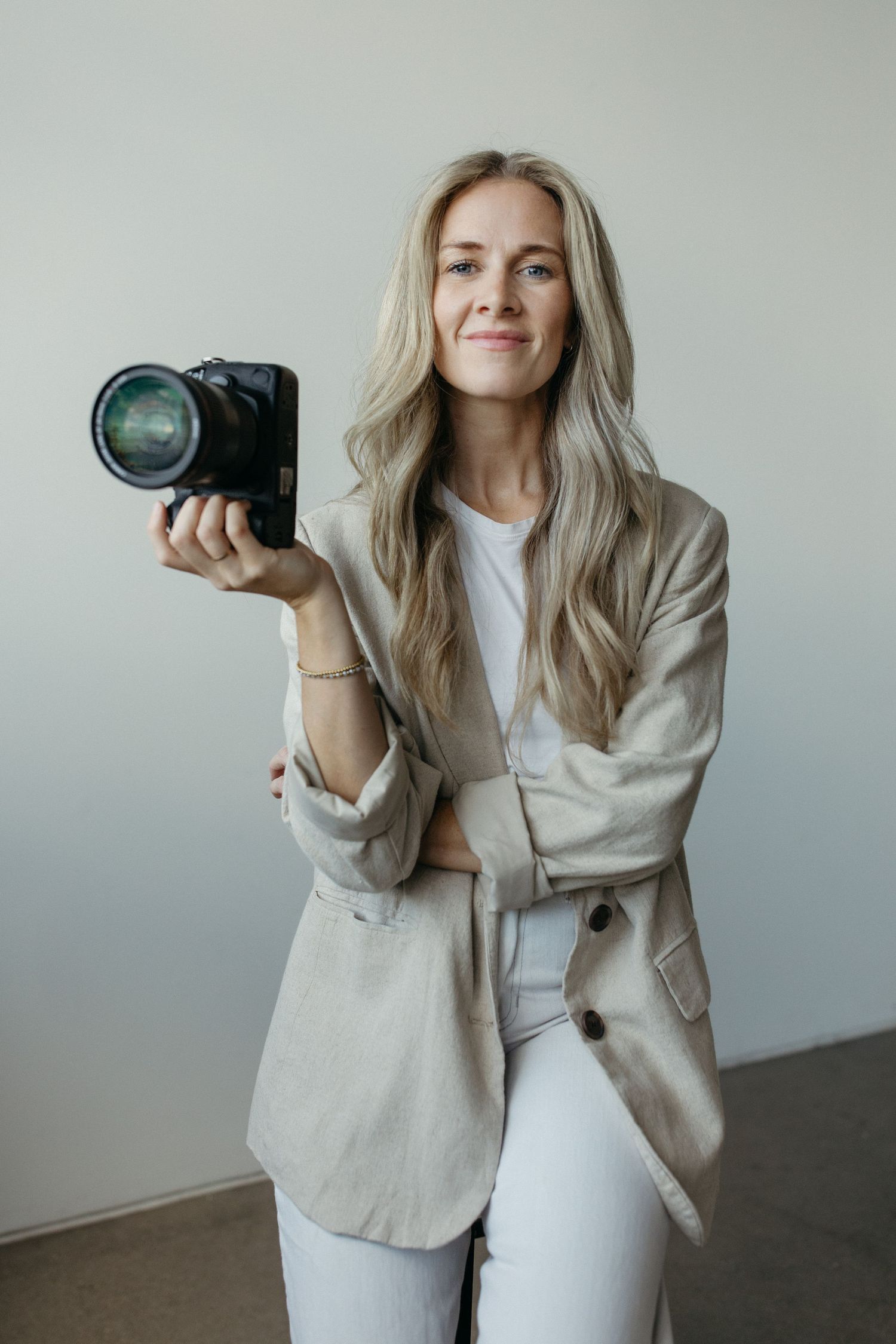 portrait photo of photographer holding a camera in her hand while sitting on a stool in a studio