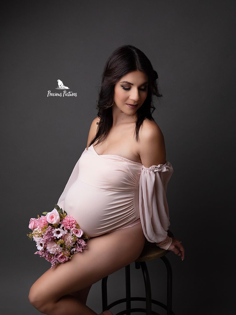 Romantic studio maternity portrait with a pink floral bouquet and off-the-shoulder bodysuit by Precious Pictures photography, Malta.