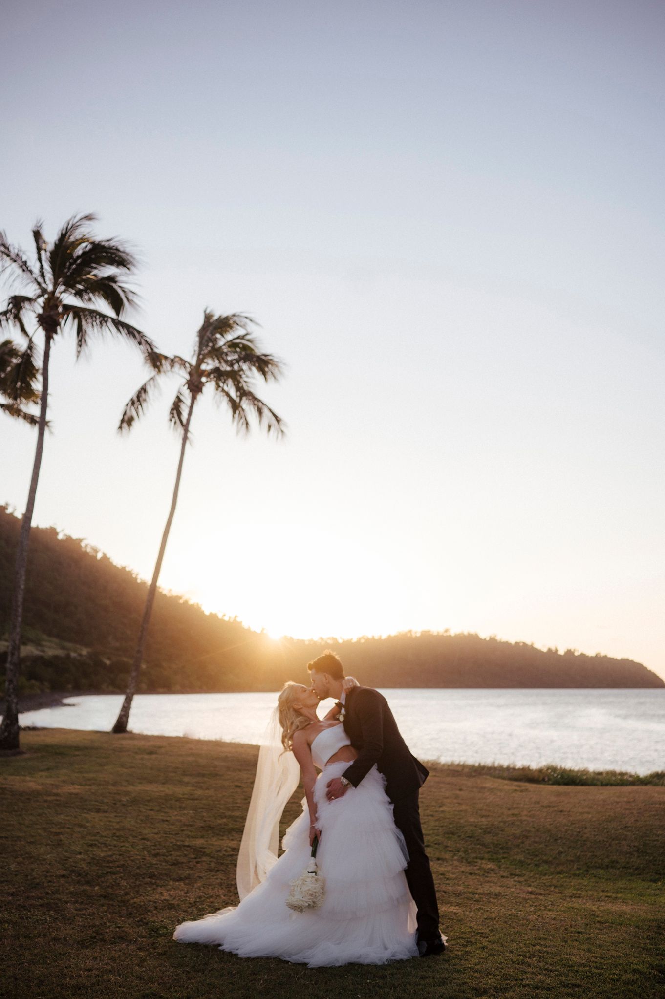Romantic beach wedding scene with palm trees and ocean backdrop at sunset.