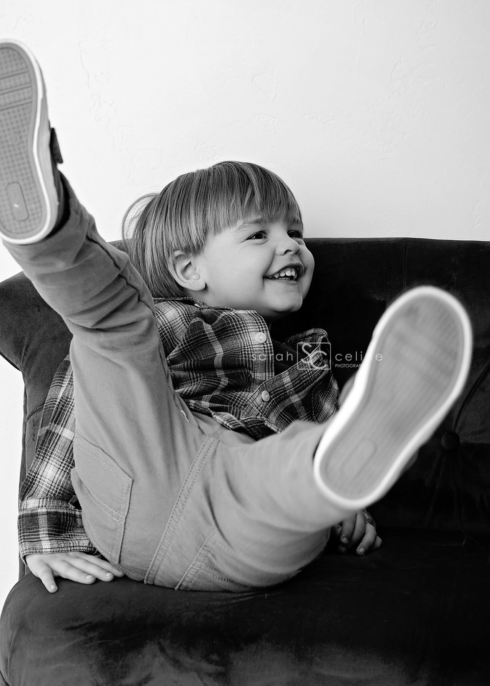 Black and white photo of a joyful child laying back on a couch with legs raised up in a playful pose.