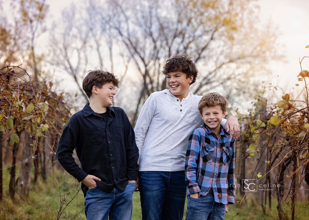 Three people laughing and walking together in a wooded autumn setting with golden leaves and natural light.