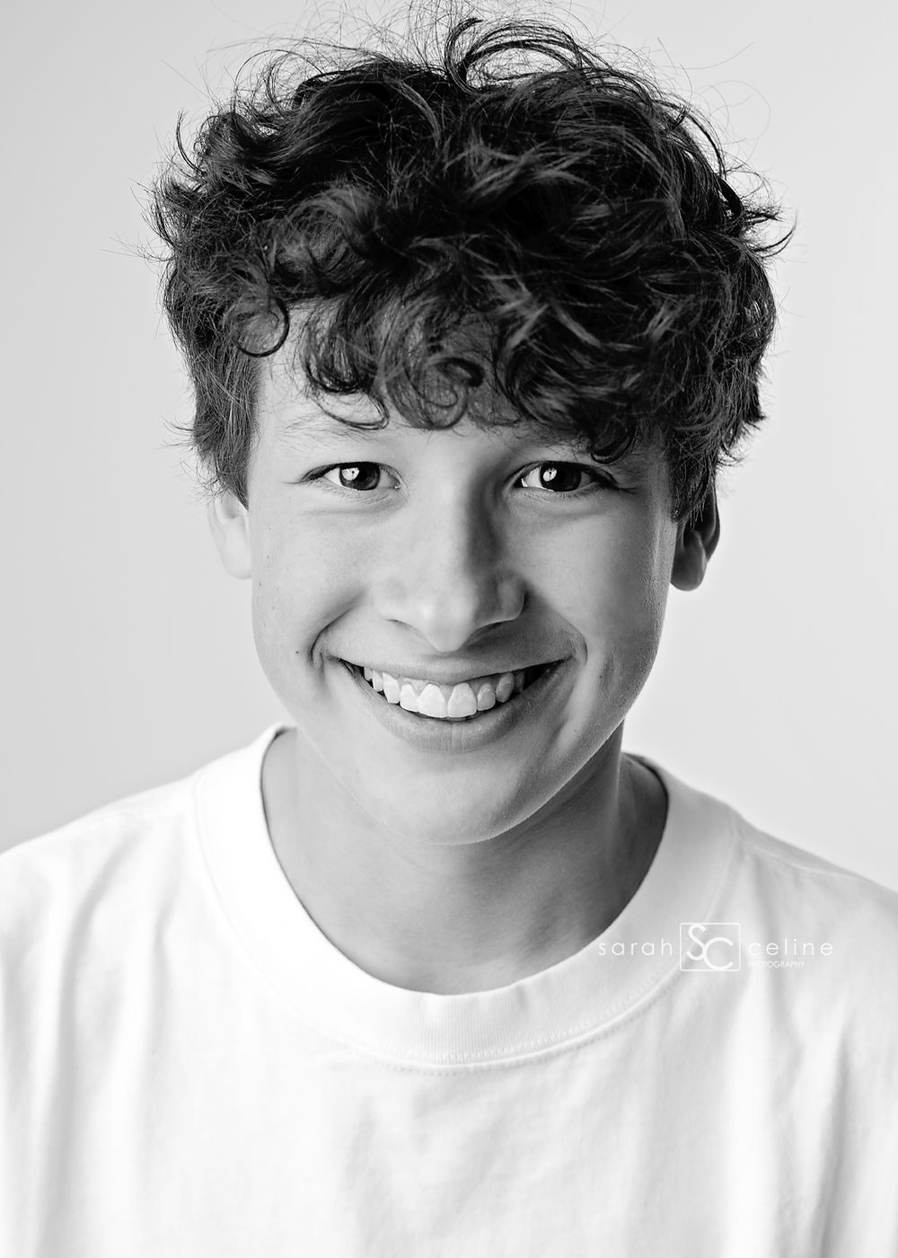 Black and white portrait of a smiling teenage boy with curly hair wearing a white t-shirt.