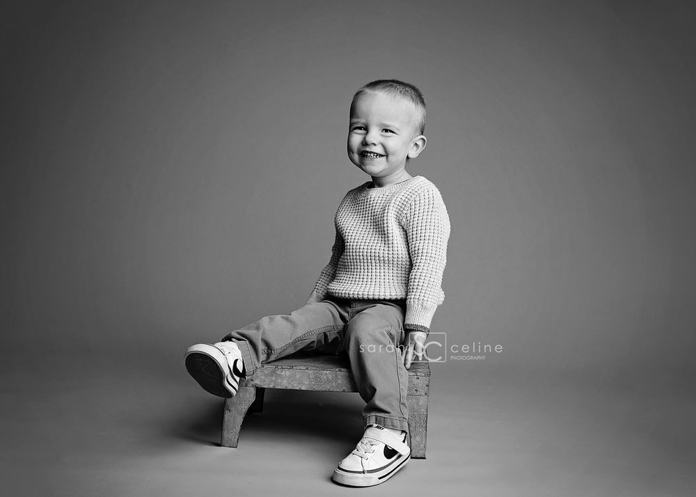 Black and white artistic photo series showing a small child sitting and playing in different poses on a light background.