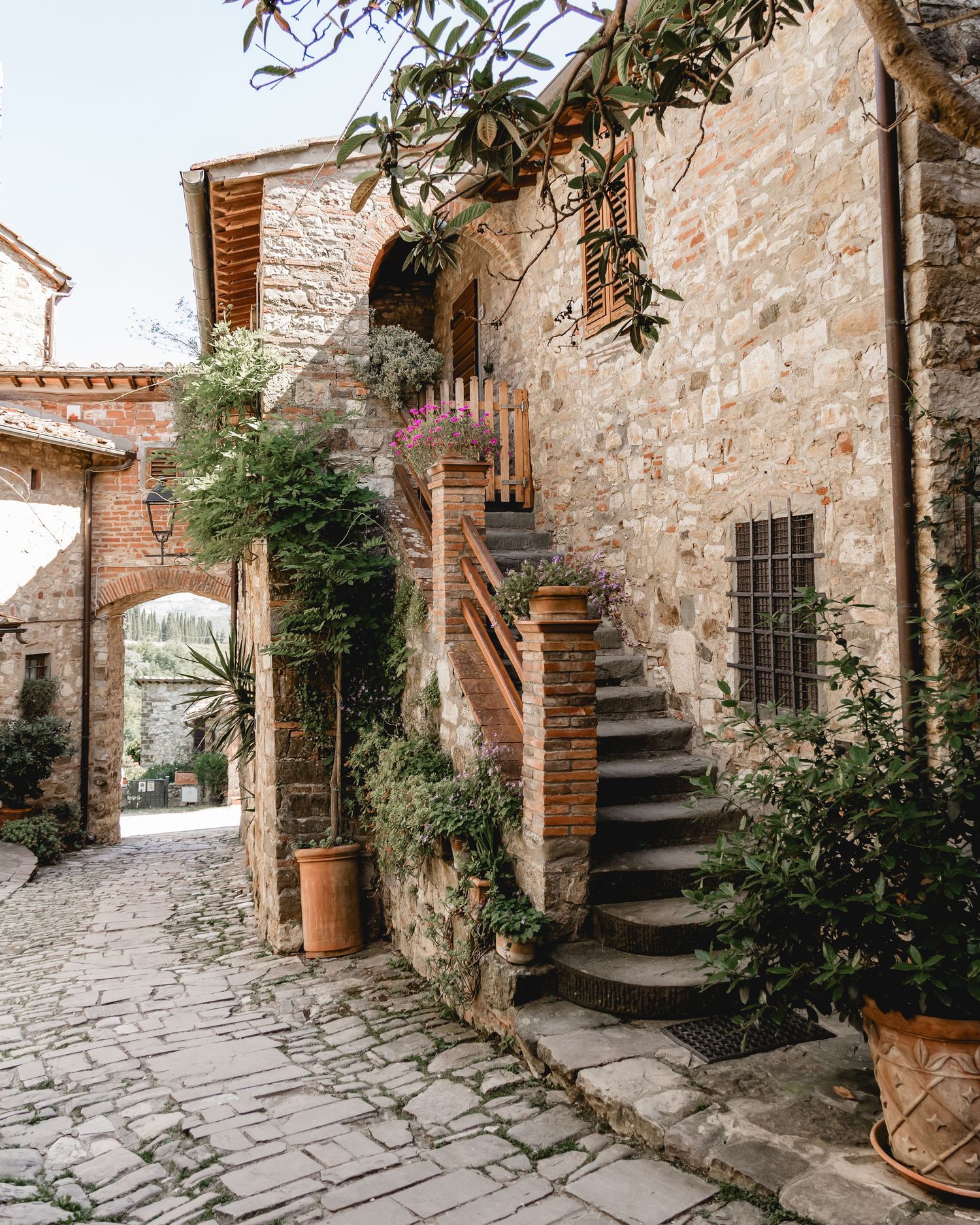 Rustic stone courtyard with wooden stairs and potted plants in an Italian village.