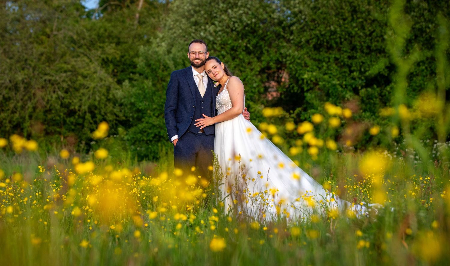 Bride and groom embracing in yellow wildflower meadow on wedding day.