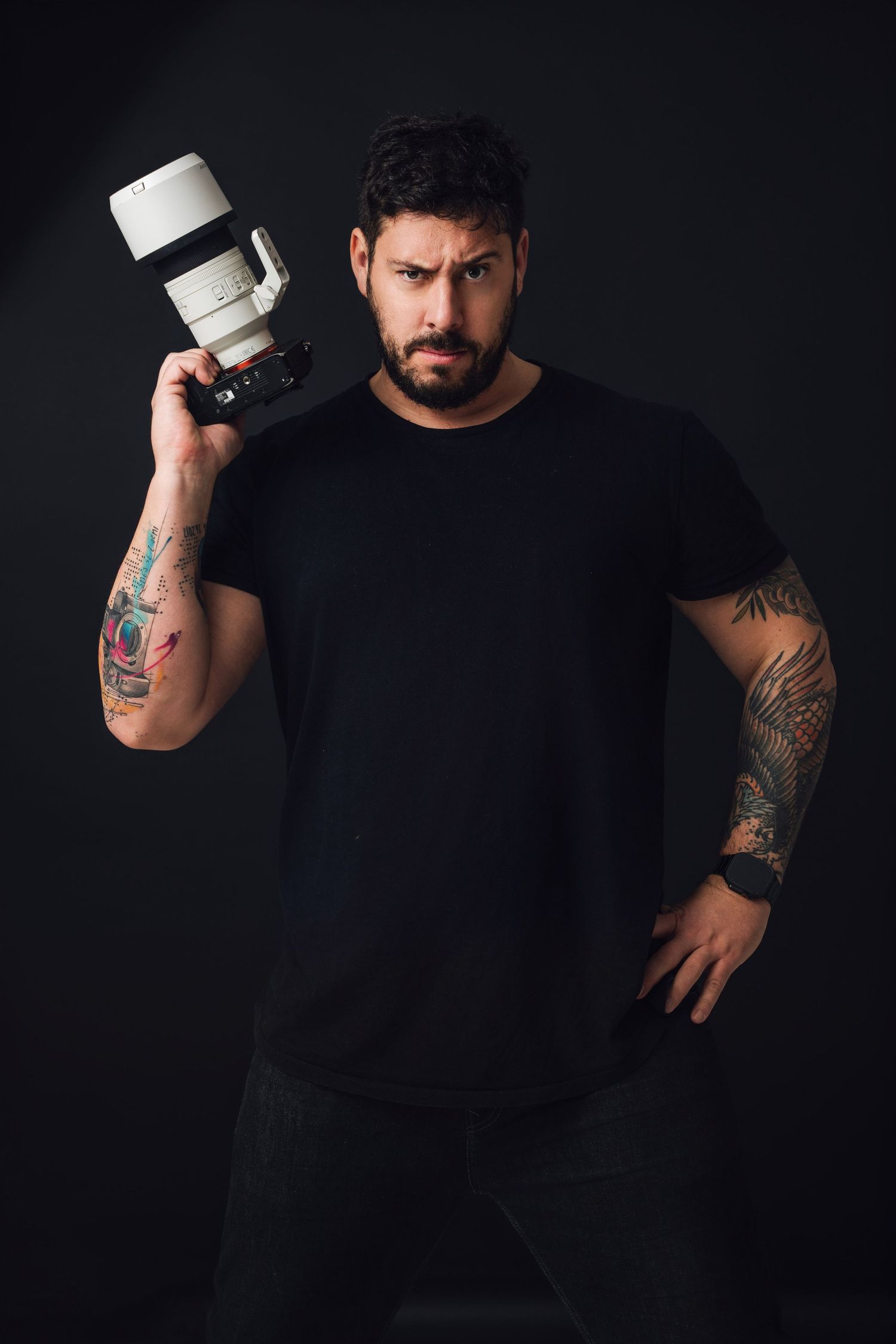 Professional photographer in black shirt holding white telephoto lens against dark background.