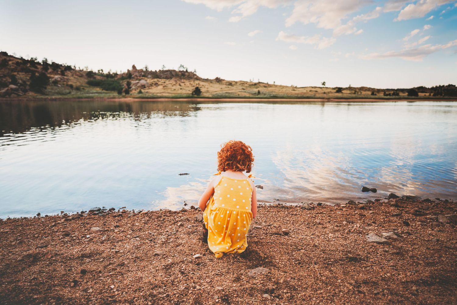 Little girl with red hair sits in front of lake reflecting the clouds in Dickson, TN
