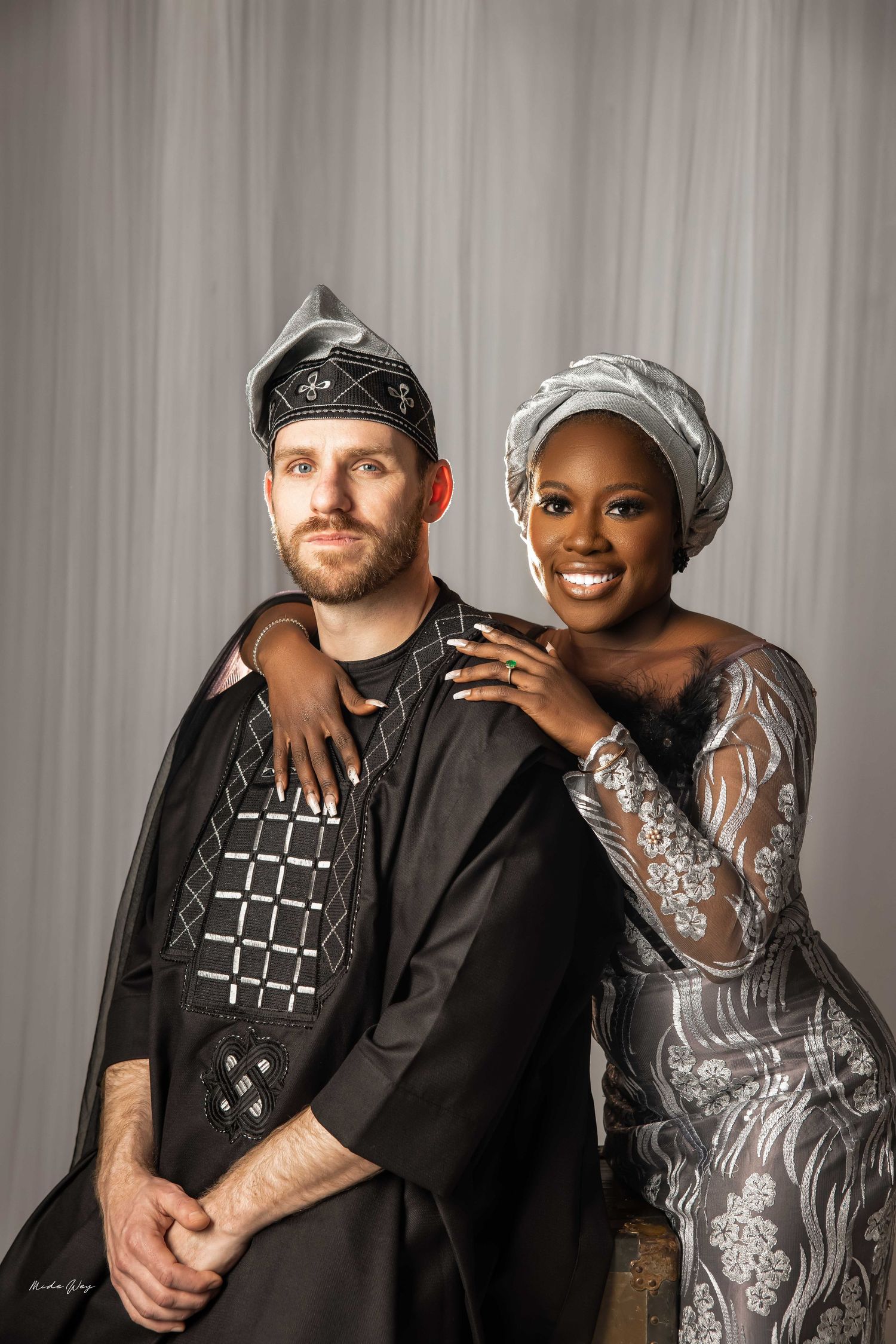A couple poses together in studio portrait wearing black and silver outfits with coordinated headwear.