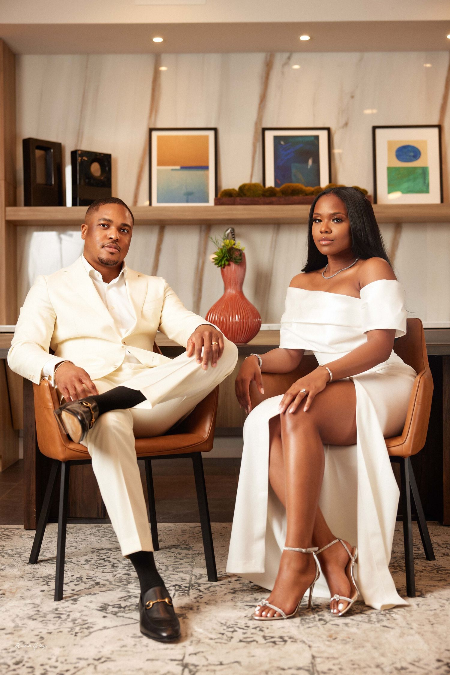 A series of five connected photos showing a couple in white outfits posing on brown chairs against a modern art gallery wall.