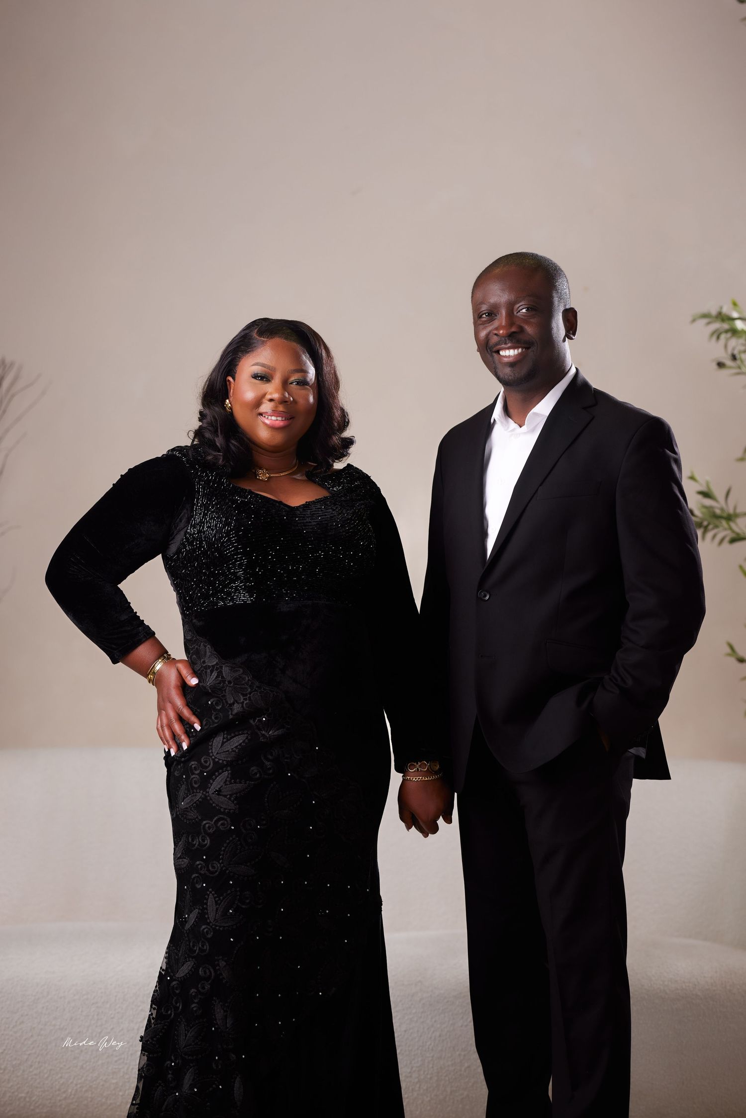 A couple poses together in formal black attire for a series of elegant portrait photos against a neutral background.