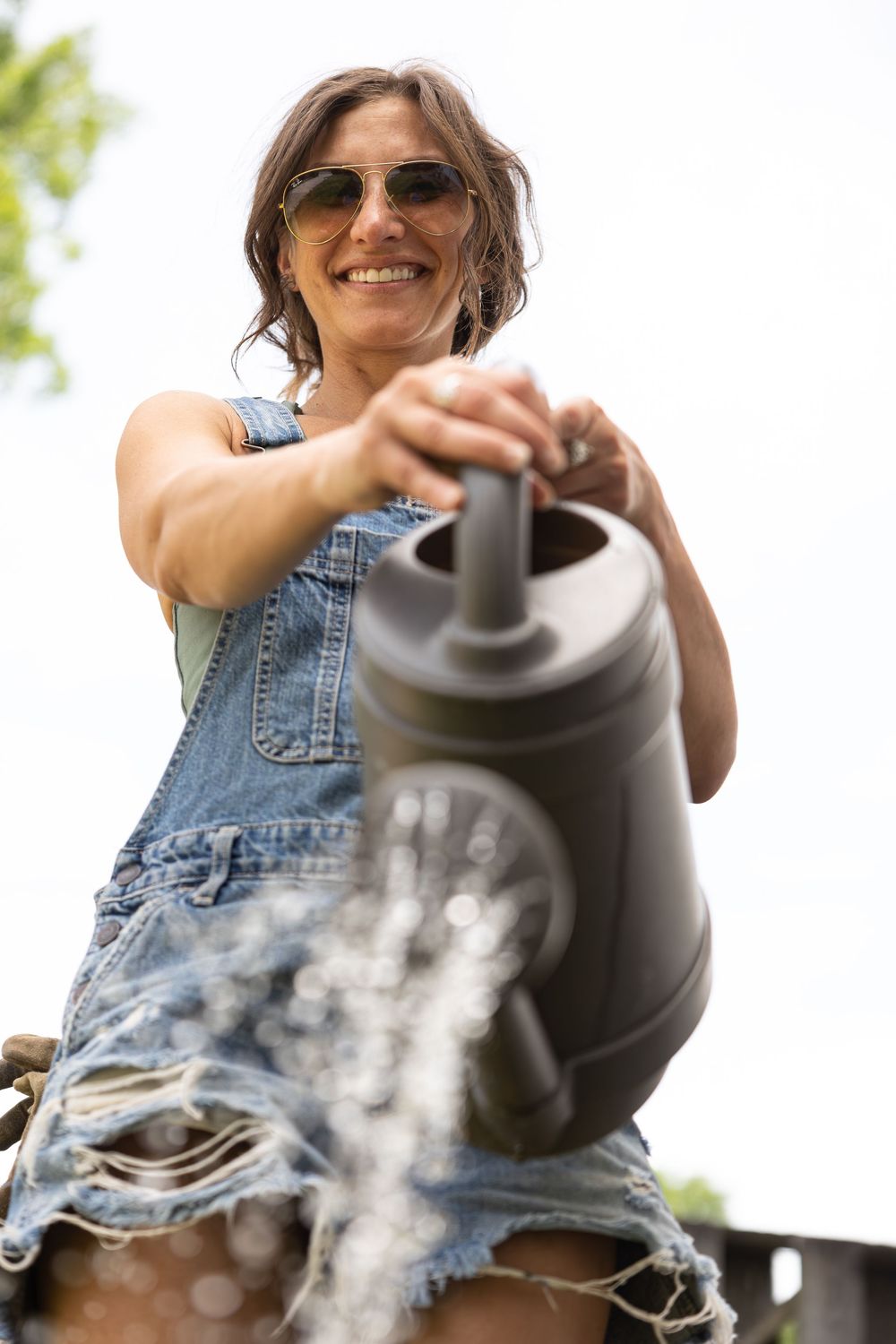 Person in denim vest pouring from a steaming kettle outdoors.