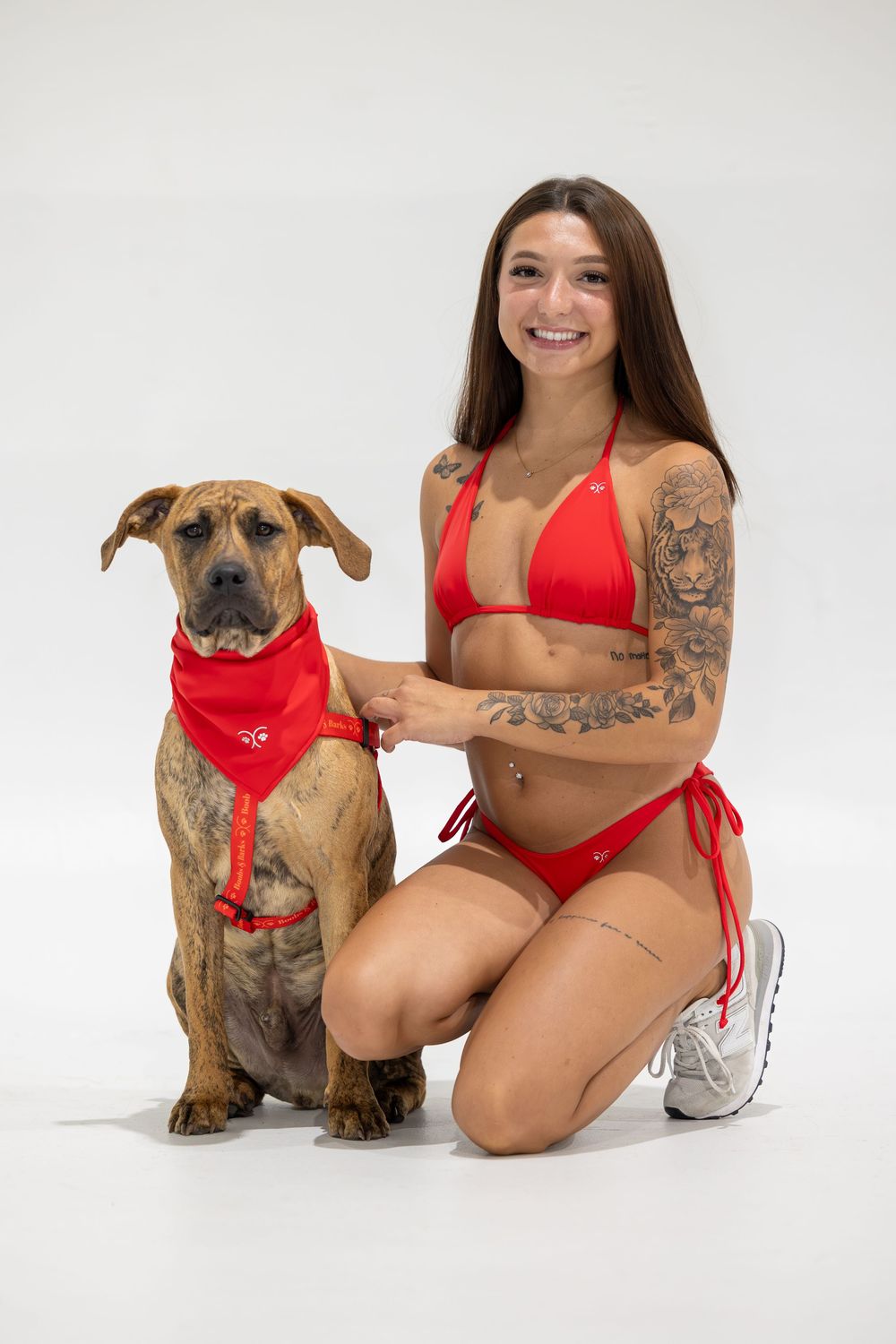 Person in red swimwear posing with brown dog wearing matching red bandana.