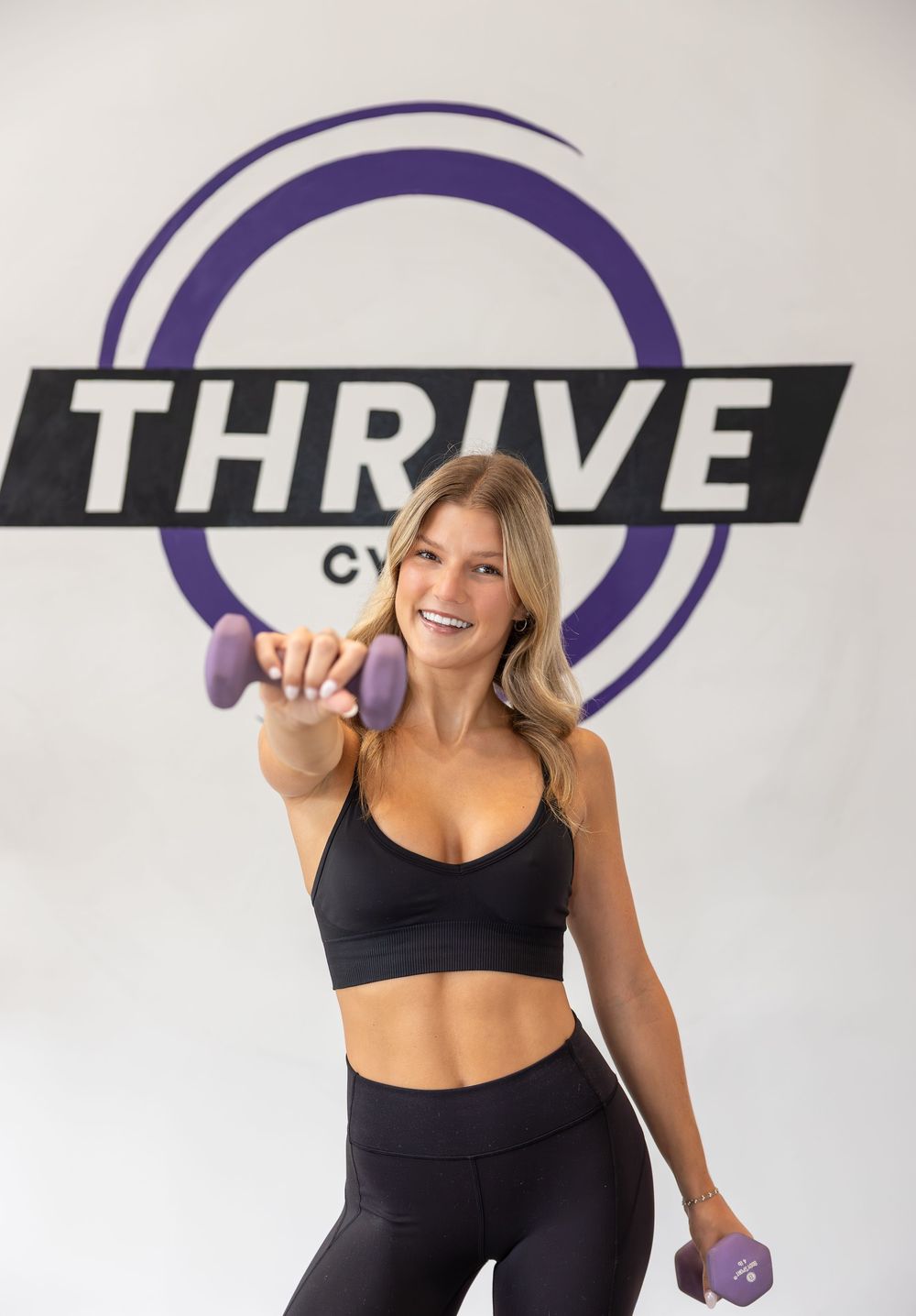Fitness instructor demonstrating workout moves in black athletic wear against branded wall.