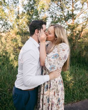 Romantic couple embracing in a floral dress and white shirt against natural scenery.