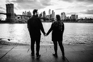 Silhouetted couple walking along waterfront with city skyline in background.