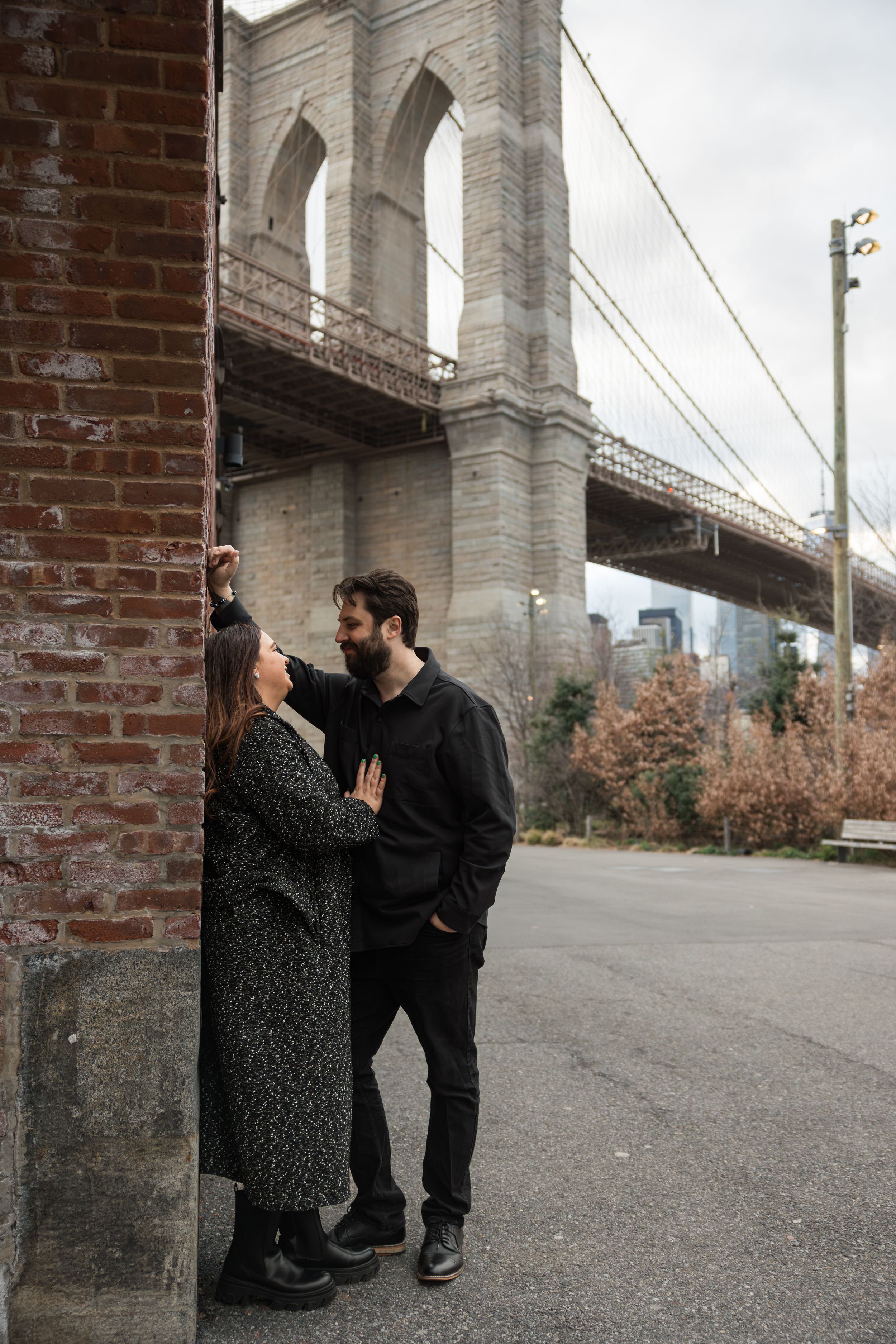 Couple sharing an intimate moment under a large stone bridge in an urban setting.