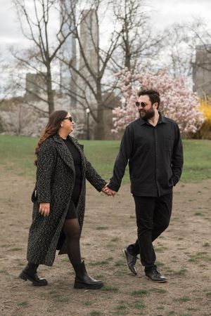 A playful couple poses in a park setting with spring blossoms and casual outfits.